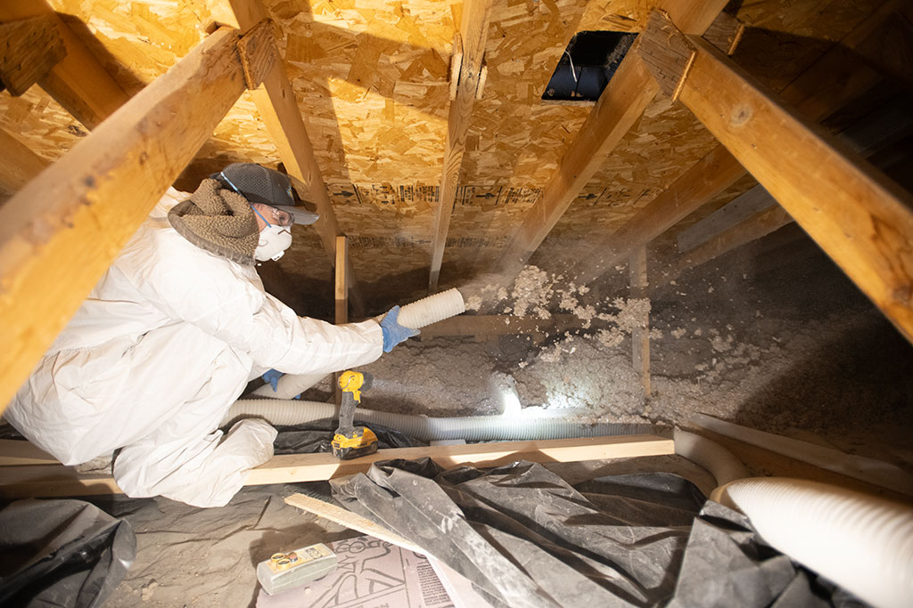 worker in attic holding a hose that is being used to spray insulation into the attic