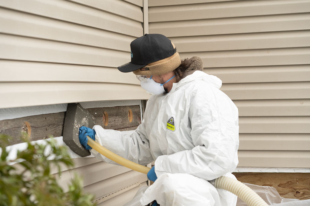 worker outside of a home holding a hose being used to pump insulation into the home