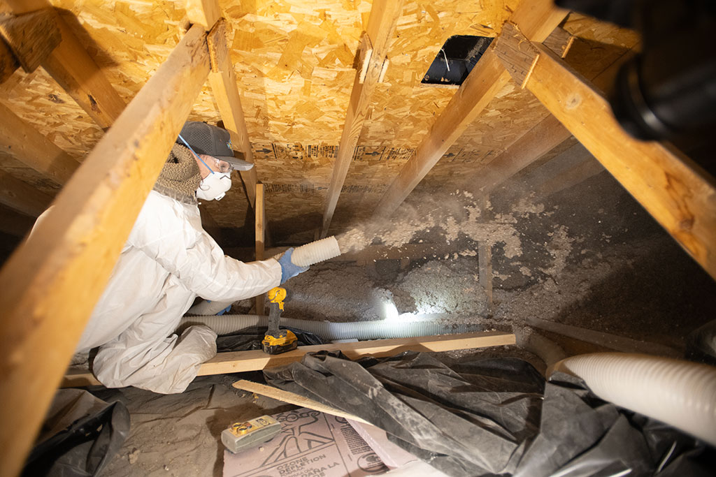 worker in attic holding a hose that is being used to spray insulation into the attic