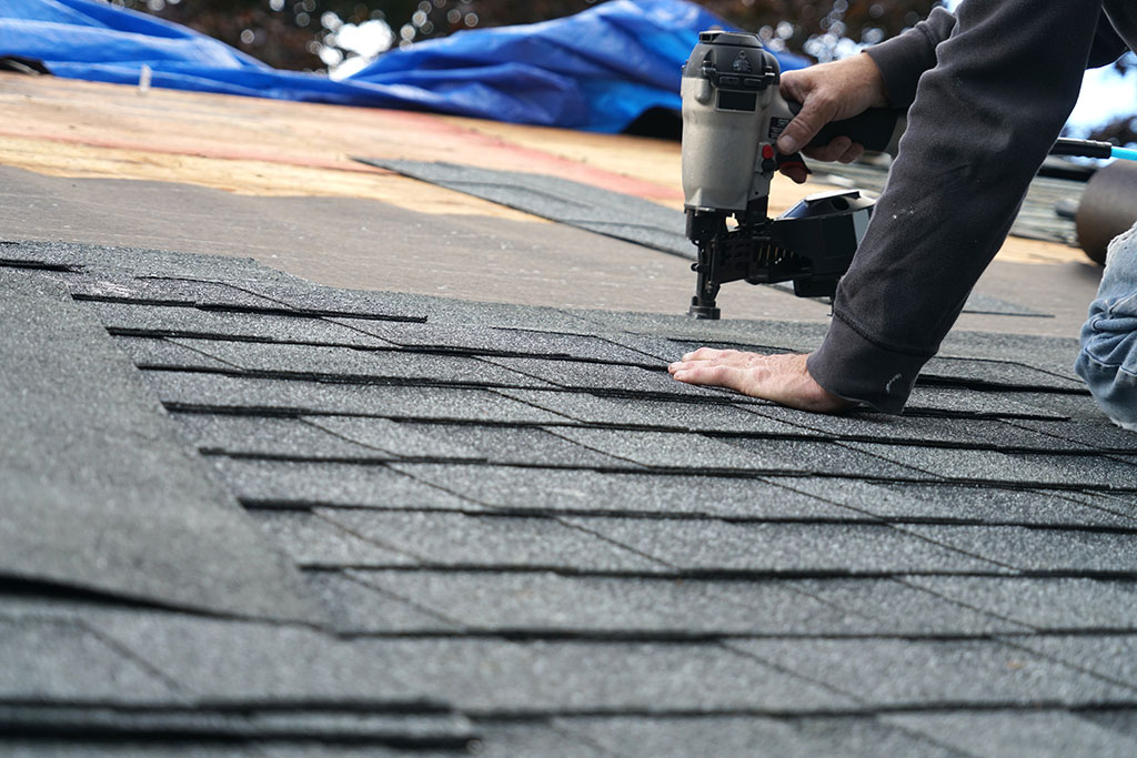 worker nailing shingles into place on a roof