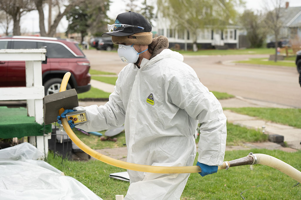 a WxForce team member dressed in protective gear walking into a home holding a hose used to apply insulation