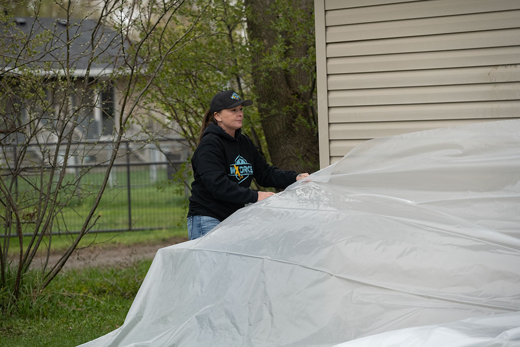 female WxForce team member adjusting a tarp that has been placed to protect items next to a home